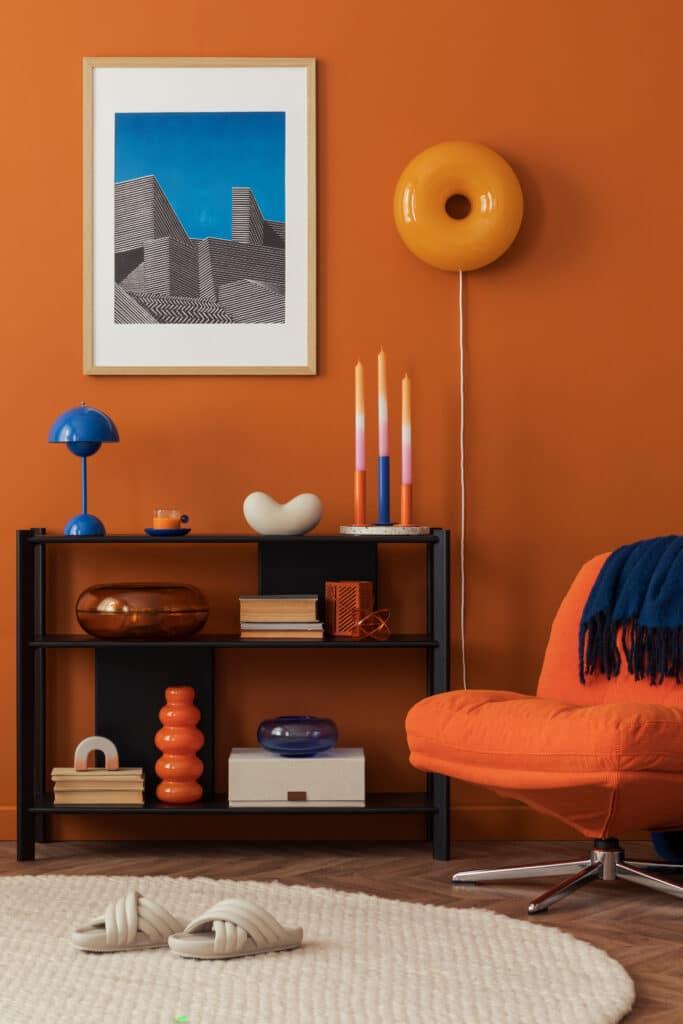 Close-up of modern orange lounge chair and bookshelf against a bold terracotta wall in a cozy home setting...