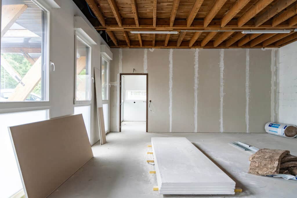 Intérieur en construction avec plaques de plâtre, isolation, et plafond à poutres apparentes, en attente de finition.